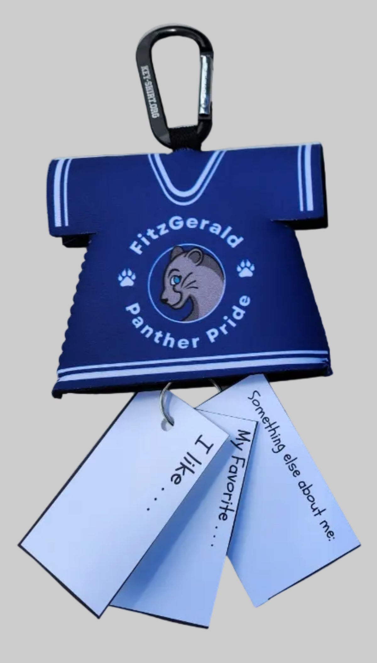 A navy blue koozie with white text reading 'Silver Panda Pride Panther' and a panda graphic, shown on a round marble table. A black carabiner is attached on the left, and two white tags are attached on the right.
